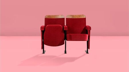 Twee rode stoelen met houten armleuningen staan tegen een roze achtergrond.