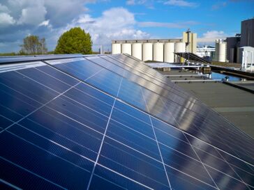 Zonnepanelen op een dakterras met een blauwe lucht en wolken op de achtergrond.