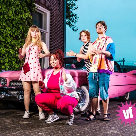 Groep jonge mensen poseren voor een roze auto, met kleurrijke outfits en een levendige sfeer.