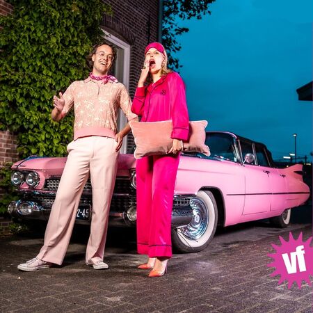 Man en vrouw in retro kleding bij een roze auto, met een speelse en vrolijke uitstraling.