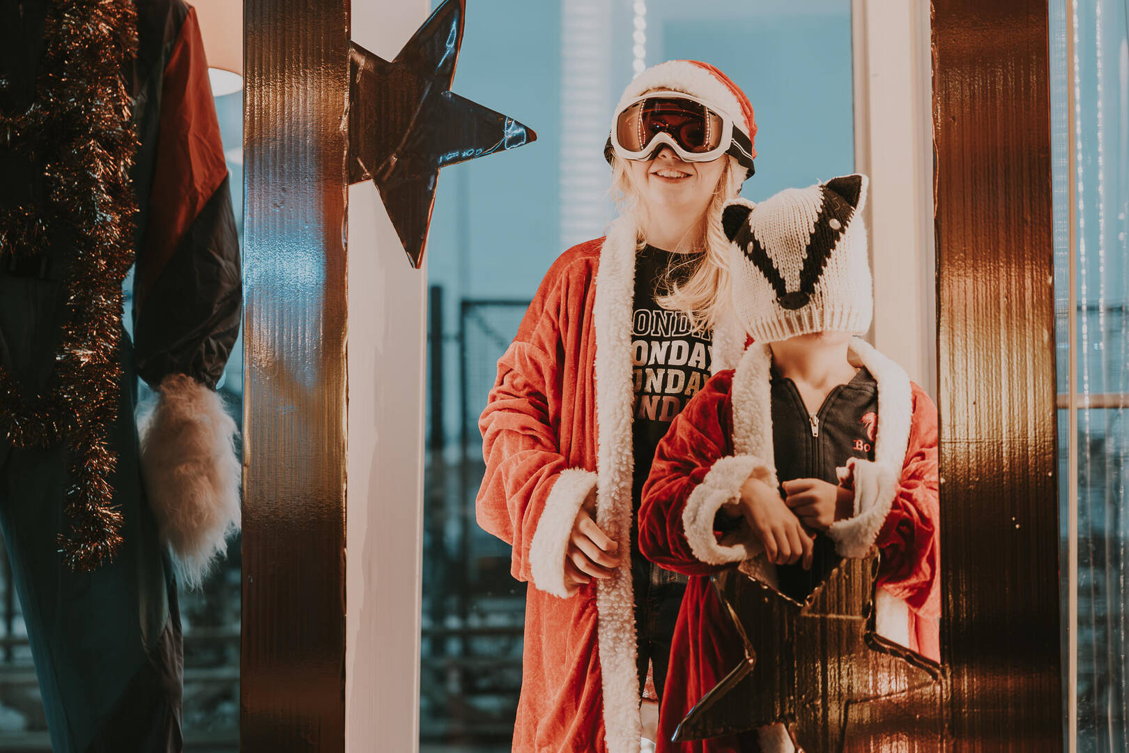 Twee kinderen in feestelijke kleding, één in een kerstman-outfit, met kostuums en accessoires in een speelse setting.