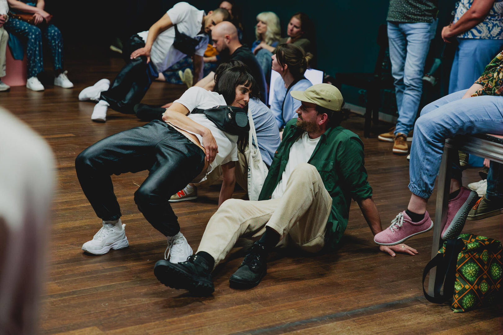Mensen zijn bezig met een dansactiviteit in een zaal, met één persoon op de vloer in een creatieve pose.