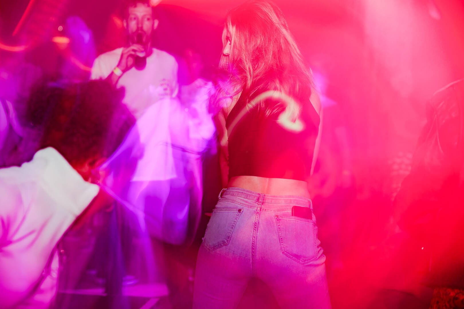 Een vrouw danst in een club met kleurrijke verlichting, omringd door andere feestgangers.