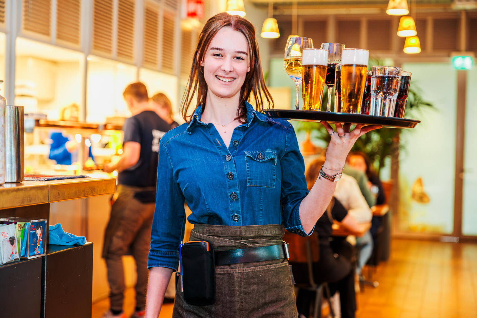 Een serveerster houdt een dienblad met glazen drinken vast in een druk restaurant.