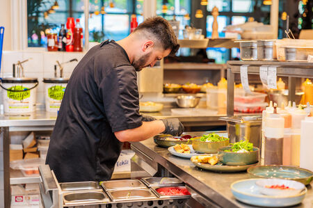 Een chef-kok in een keuken bereidt gerechten op een werkblad met verschillende ingrediënten en schalen.