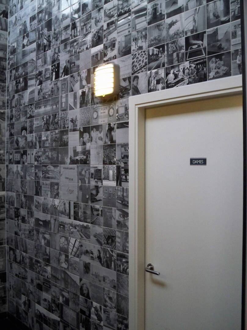 Een muur bedekt met zwart-wit foto’s en een deur met een naambordje ernaast.