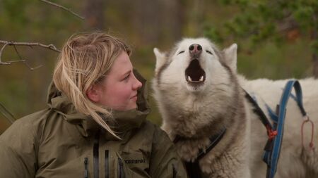 Vrouw kijkt naar een hondsachtige die een lange huil laat horen in een natuurlijke omgeving.