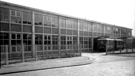 Zwart-witfoto van een groot schoolgebouw met veel ramen en een oprit.