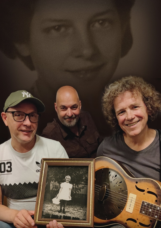 Drie mannen poseren met een foto van een meisje, met een zwart-wit portret op de achtergrond.