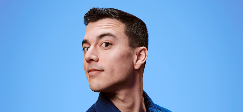Jonge man met een korte haarstijl kijkt over zijn schouder tegen een helderblauwe achtergrond.