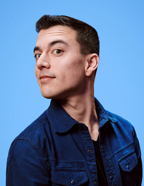 Portret van een man met kort bruin haar en een blauwe achtergrond, kijkend over zijn schouder met een neutrale uitdrukking.