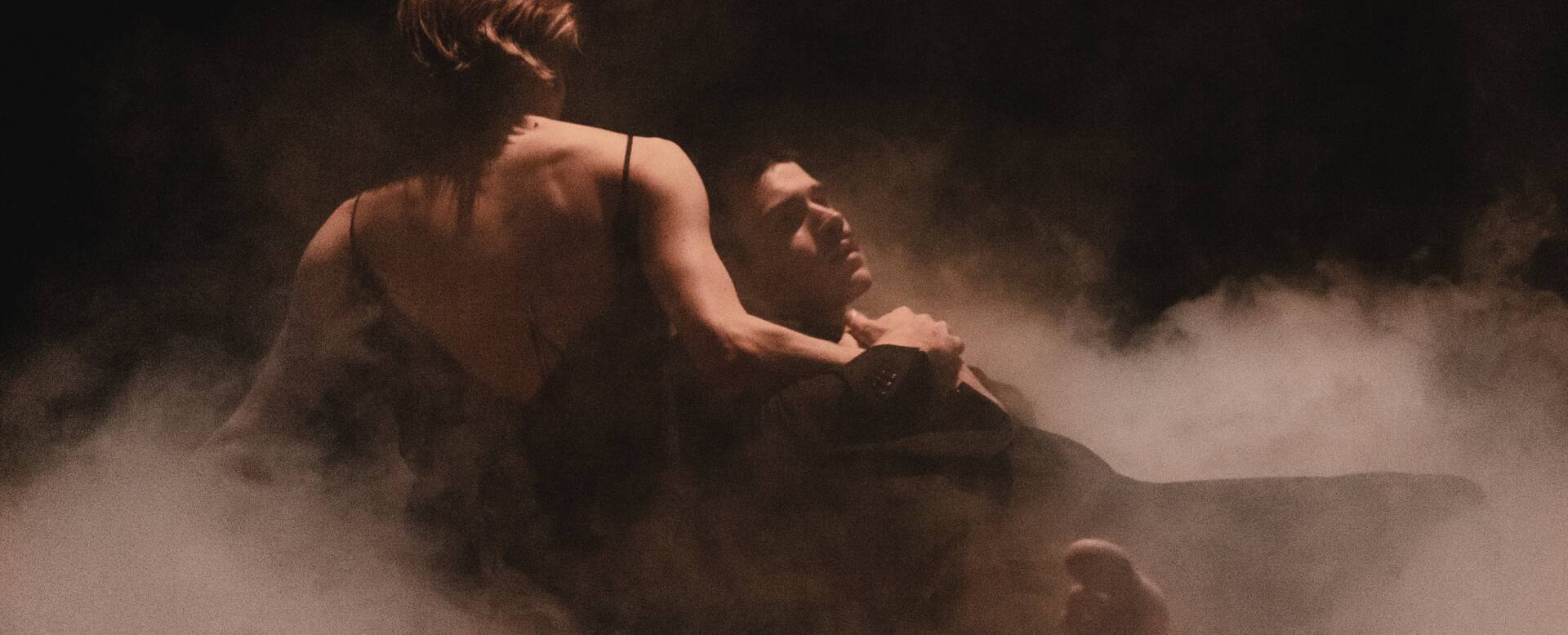 Twee dansers in een mistige setting, één houdt de ander vast, wat een krachtige emotionele expressie uitstraalt.