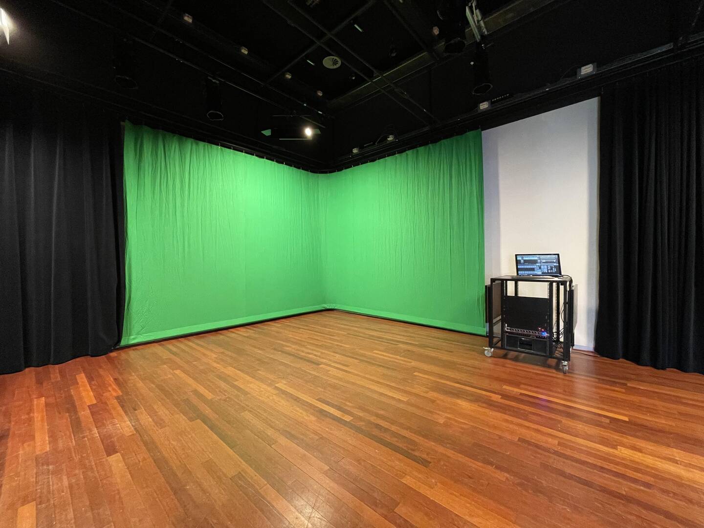 Lege ruimte met groene backdrop, geschikt voor videoproducties, met een houten vloer en een apparaat op een wagen.