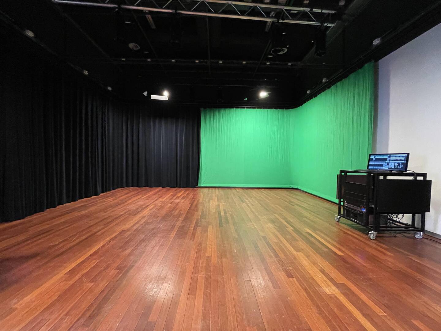 Leeg filmstudio-interieur met houten vloer, zwarte gordijnen en een groene schermwand. Aan de zijkant een computerstation.