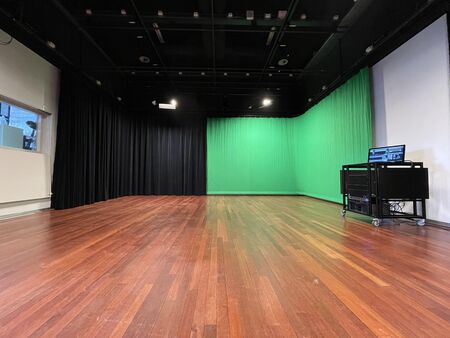 Lege opnamestudio met een groene schermwand en houten vloer, voorzien van spotlights 