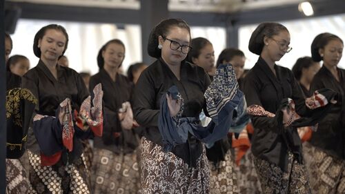 Vrouwen in traditionele kleding voeren een culturele dans uit, met kleurrijke stoffen in hun handen.