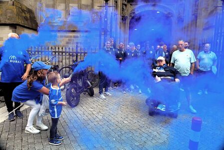 Een jong kind en een volwassene met een rolstoel afgevuurd blauwe rook tijdens een feestelijke bijeenkomst, omringd door anderen.