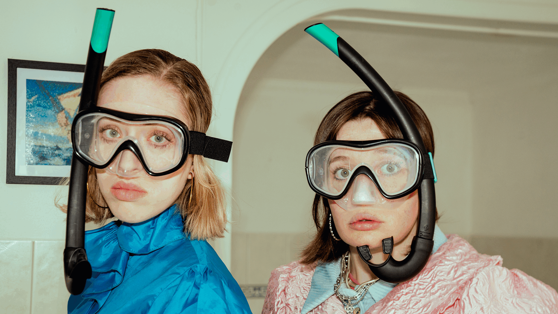 Twee mensen staan in zwemuitrusting met snorkels en duikbrillen, met een verwonderde uitstraling in een binnenruimte.