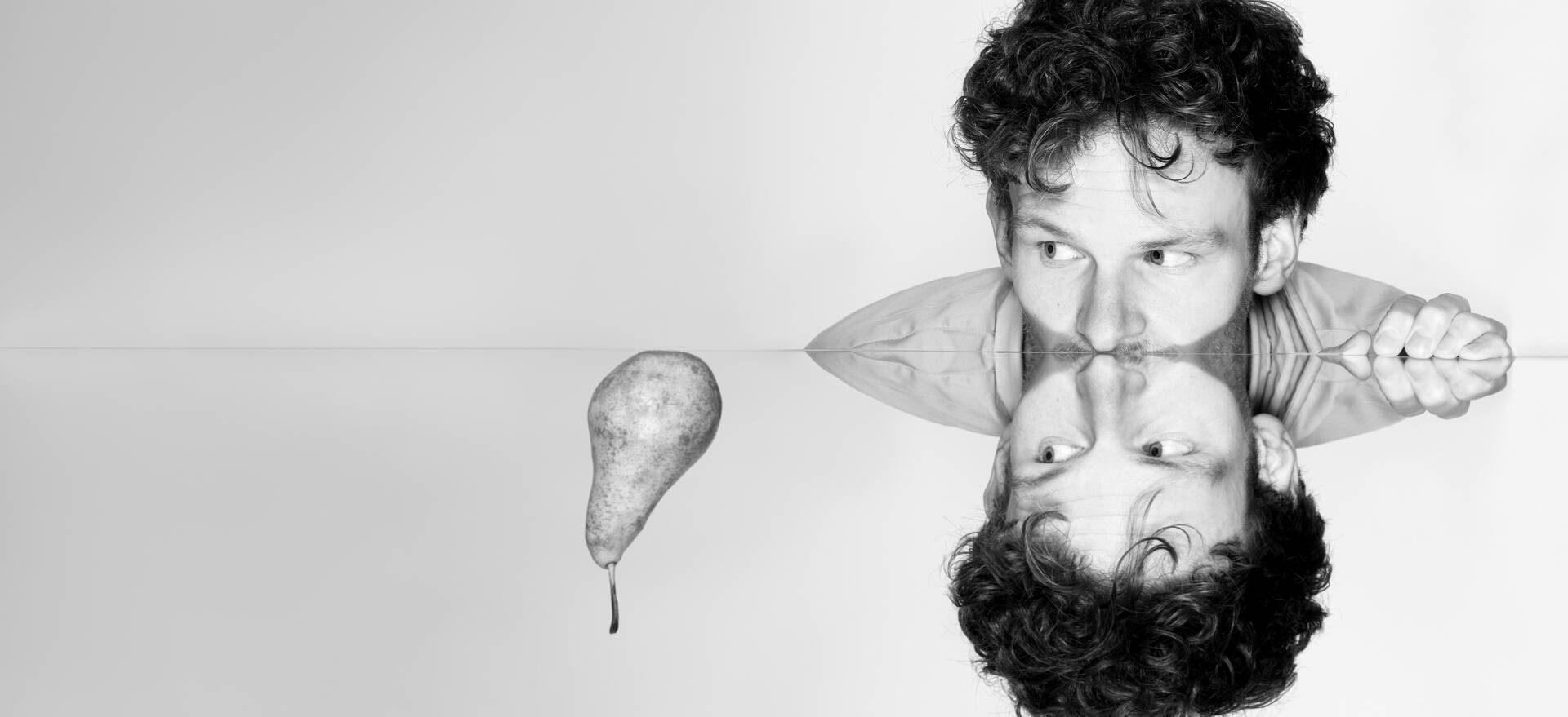 Zwart-wit afbeelding van een persoon met een reflectie in water naast een perenillustratie.
