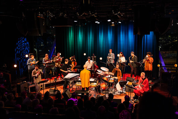 Een jazzband met diverse muzikanten speelt op een podium met kleurrijke verlichting voor een enthousiast publiek.