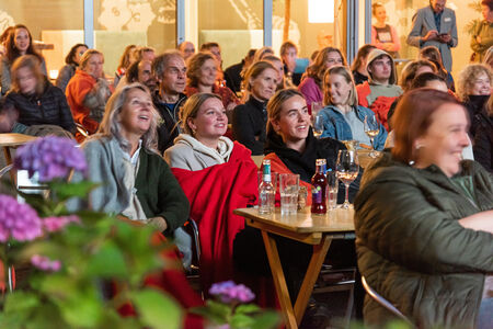 Een groep mensen kijkt aandachtig naar een presentatie in een ontspannen buitenomgeving.