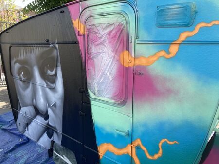Gekleurde caravan met graffiti, inclusief portret van een vrouw die een sigaret vasthoudt.