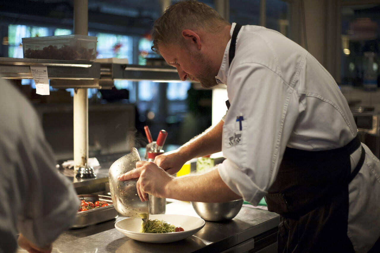 Een chef-kok bereidt een gerecht in een restaurantkeuken met aandacht voor detail.