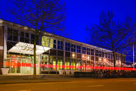 Verkadefabriek in het donker, met verlichting en bomen vooraan.