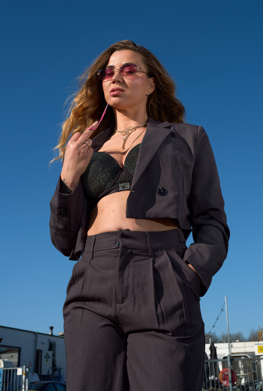 Een vrouw in een elegante zwarte outfit met zonnebril poseert onder een blauwe lucht.