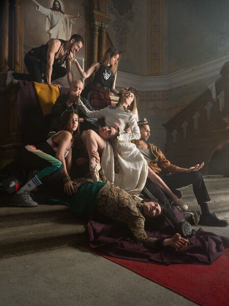 Groep mensen in kostuums poseert dramatisch op een trap in een historische, sfeervolle omgeving.