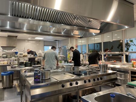 Drie koks werken in een moderne professionele keuken met verschillende kooktoestellen en keukengerei.