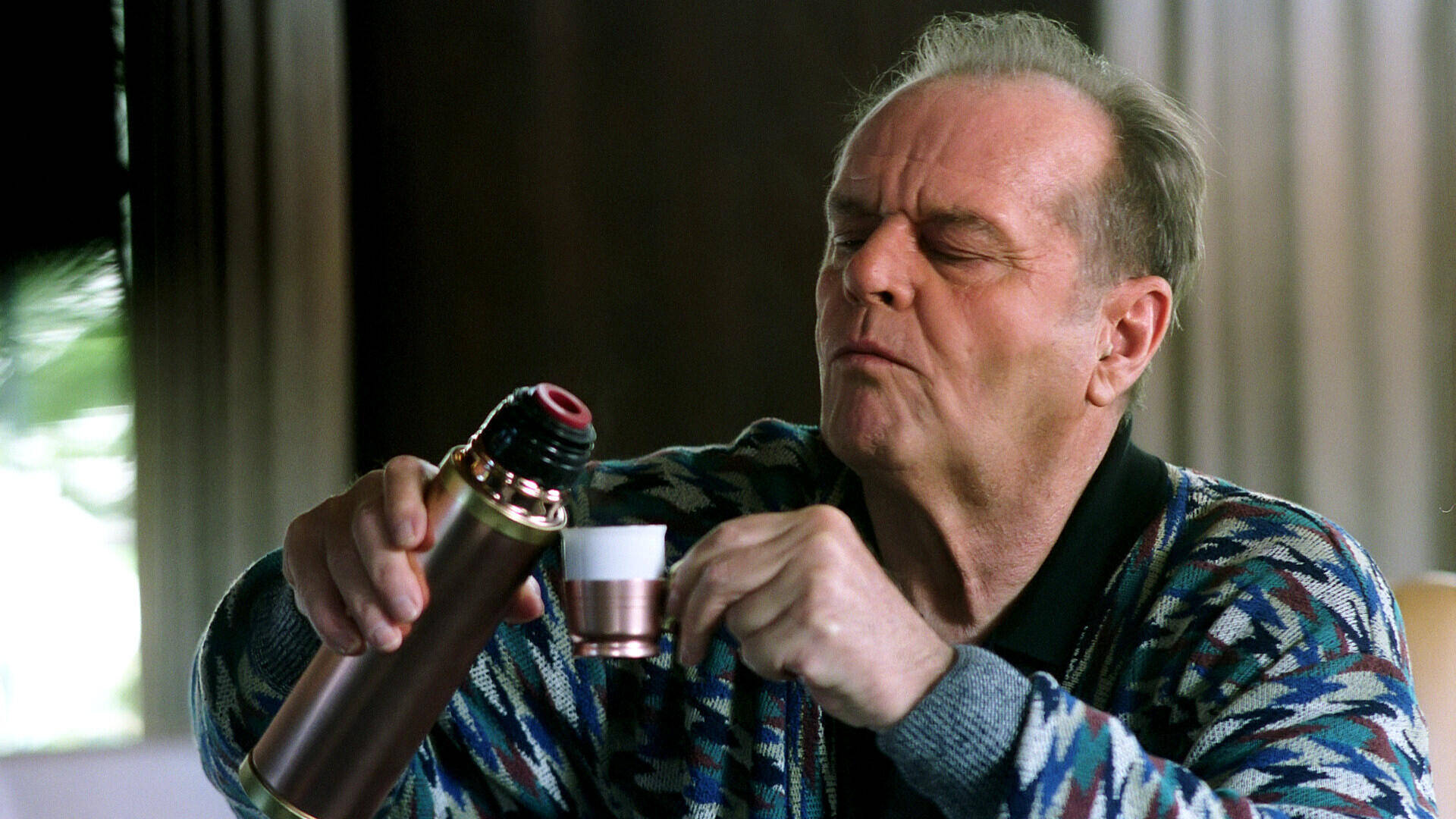 Acteur Jack Nicholson in een kleurrijke trui schenkt koffie uit een thermoskan in een klein kopje.
