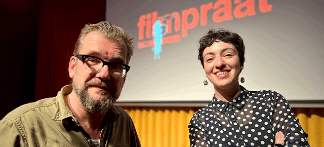 Twee mensen poseren voor een podium met het logo van "filmpraat" op de achtergrond.