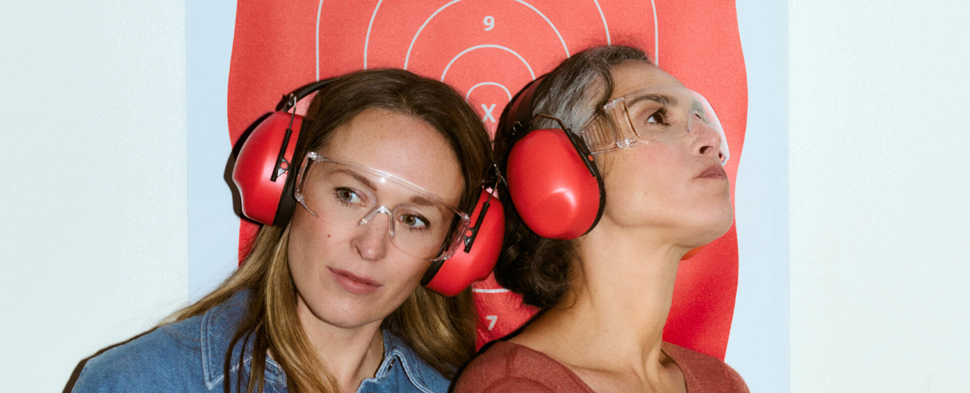 Twee vrouwen met gehoorbescherming kijken naar een schietschietschijf op de achtergrond.