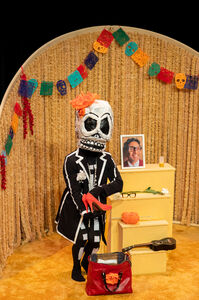 Decoratieve afbeelding van een skelettumpop in een feestelijke setting, met een foto en versieringen voor Día de los Muertos.