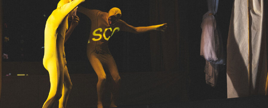 Een danser in een lichaamsbedekkend kostuum beweegt op het podium, omringd door kleurrijke doeken.