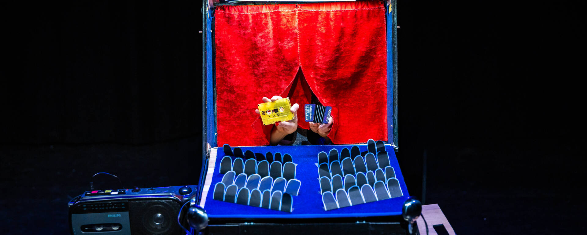 Een open koffer met een podium voor poppen, verlicht met een rode achtergrond en verschillende poppen voor een voorstelling.