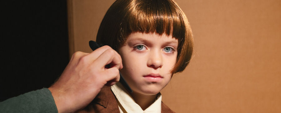 Een jonge jongen met een korte, bruin haarstijl kijkt ernstig terwijl iemand zijn haar stylt.