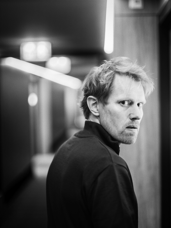 Zwart-wit portret van een man die omkijkt in een gang met zachte verlichting.