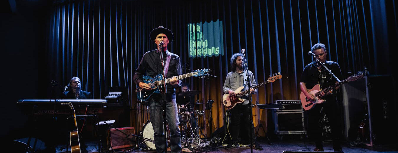 Een band speelt live op het podium met een zanger, gitarist en toetsenist in een sfeervolle zaal.