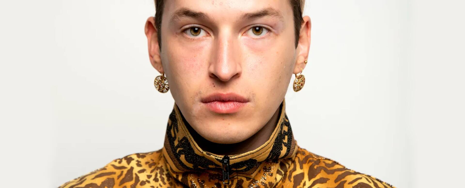 Jonge man met kort haar, gekleed in een geel met zwart gestreepte blouse, staande voor een neutrale achtergrond.