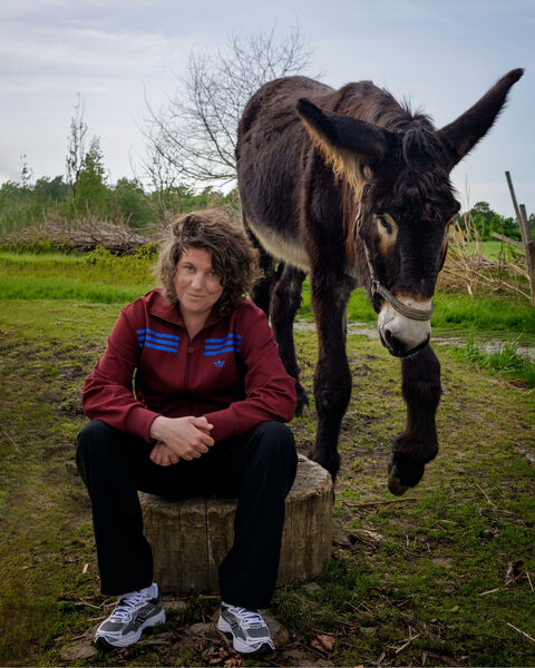 Een persoon zit op een boomstronk terwijl een ezel dichtbij staat op een grasveld.