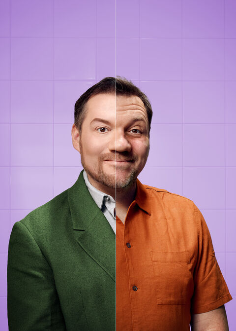 Een man met een half groene, half oranje shirt tegen een paarse achtergrond, met een lach op zijn gezicht.