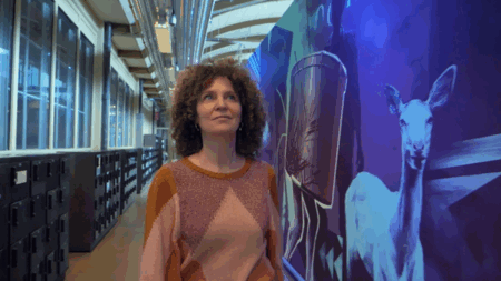 Vrouw met krullend haar loopt in een moderne ruimte met kleurrijke muurschilderingen van dieren en abstracte vormen.