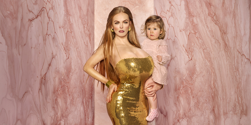 Vrouw in een gouden jurk houdt een kind vast, tegen een roze marmeren achtergrond.