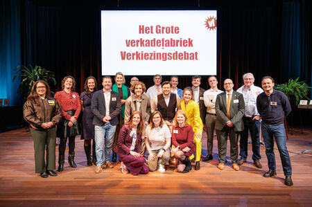Groep mensen op een podium, met een scherm op de achtergrond dat 'Het Grote Verkiezingsdebat' toont.