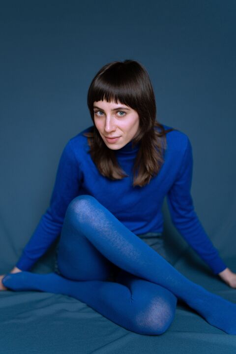 Een vrouw met lang, bruin haar in een blauwe outfit zit op een blauw oppervlak.