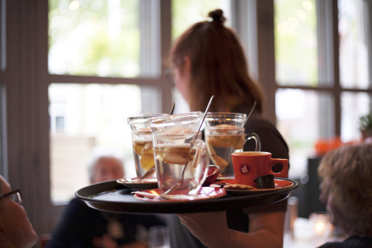 Een serveerster draagt een tray met glazen en cocktails in het restaurant.