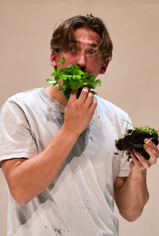 Een man met een verwarde uitstraling houdt planten vast en heeft aarde op zijn gezicht en kleding.