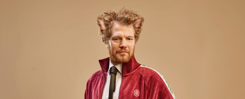 Man met een rode sportjack, stijlvolle uitstraling en kattenoren, tegen een neutrale achtergrond.